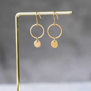 Peut inclure: Boucles d'oreilles cr&eacute;oles dor&eacute;es avec un petit disque rond suspendu &agrave; chaque cr&eacute;ole.