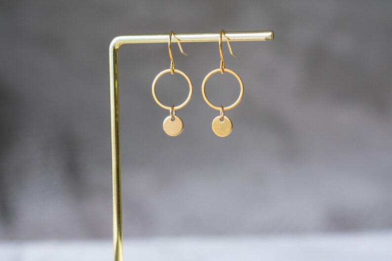 Peut inclure: Boucles d'oreilles cr&eacute;oles dor&eacute;es avec un petit disque rond suspendu &agrave; chaque cr&eacute;ole.