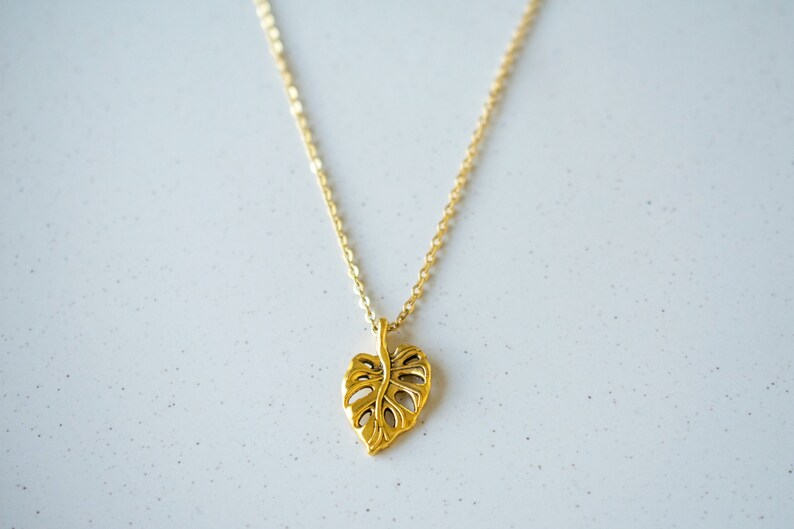 Peut inclure: Un collier en or avec un pendentif en forme de feuille d&eacute;coup&eacute;e. La feuille est un design simple et stylis&eacute;.