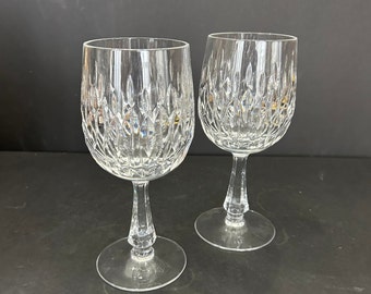May include: Two clear crystal wine glasses featuring a detailed diamond-cut pattern on the bowl. Each glass has a smooth, slender stem and a circular base, reflecting light through the intricate geometric facets etched into the glass surface.