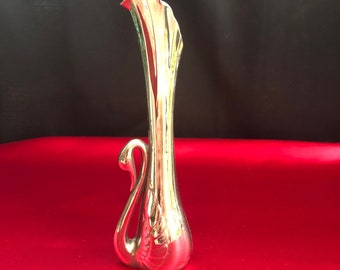 May include: A gold swan-shaped vase with a fluted neck. The vase is made of ceramic and has a shiny finish.