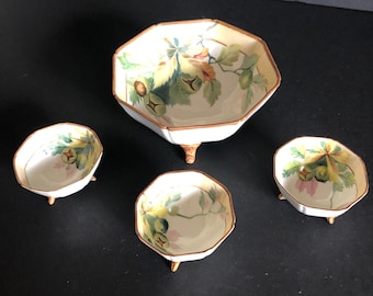 May include: A set of four antique porcelain bowls. The bowls are white with a floral design in shades of green, yellow, and brown. The rims are trimmed in gold. The largest bowl has three small feet.