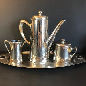 May include: A silver hammered metal tea set with a teapot, creamer, sugar bowl, and tray.