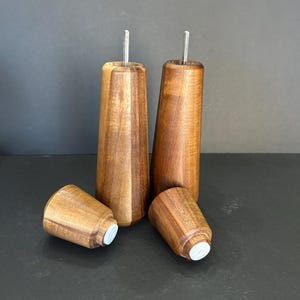 Pu&ograve; includere: Quattro gambe per mobili in legno con un design affusolato. Le gambe sono in legno marrone scuro e hanno un inserto in metallo nella parte superiore. La parte inferiore di ogni gamba ha un cappuccio in plastica bianca.