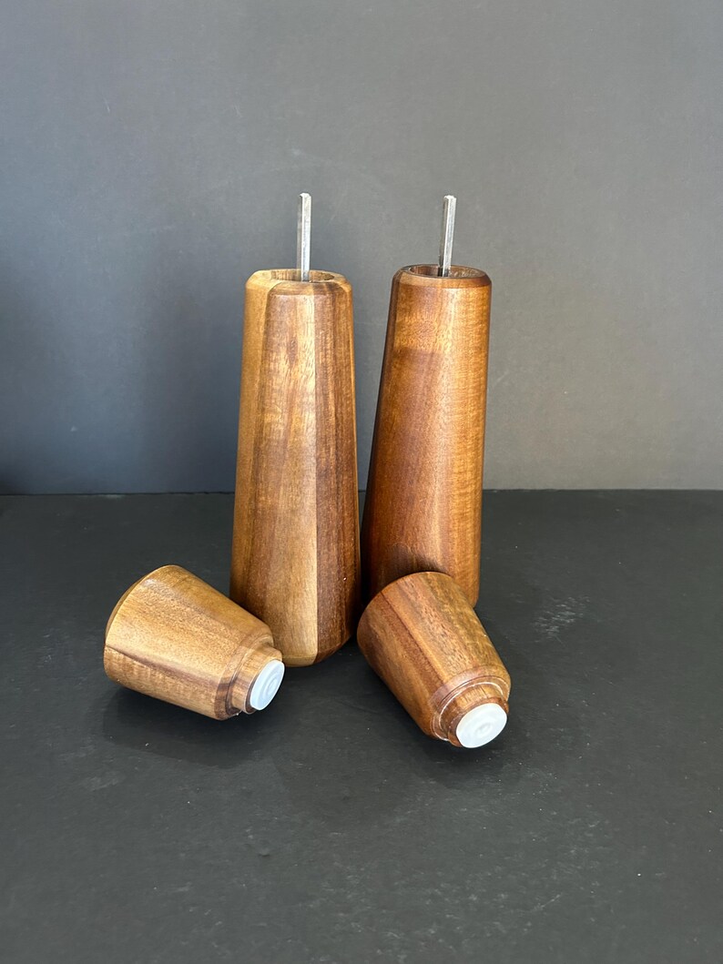Pu&ograve; includere: Quattro gambe per mobili in legno con un design affusolato. Le gambe sono in legno marrone scuro e hanno un inserto in metallo nella parte superiore. La parte inferiore di ogni gamba ha un cappuccio in plastica bianca.