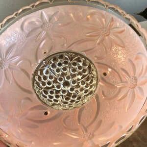 Puede incluir: Una l&aacute;mpara de techo de cristal rosa con un dise&ntilde;o floral y un centro de cristal transparente.