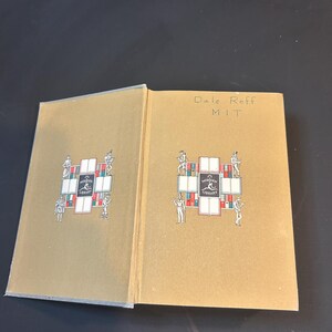 Peut inclure: Un livre ouvert avec une couverture beige orn&eacute;e d'un motif d&eacute;coratif avec des personnages et les mots "MODERN LIBRARY". La page de droite porte l'inscription "Dale Roff MIT". Le livre est sur une surface sombre.