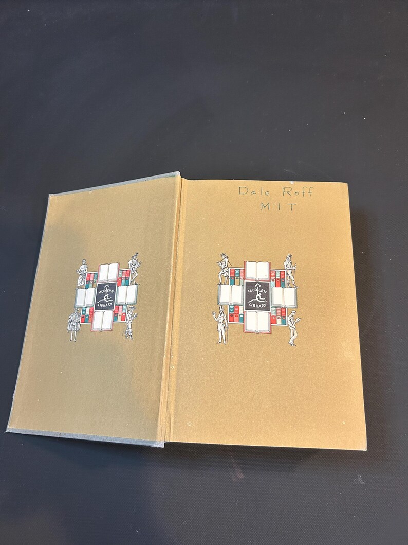 Peut inclure: Un livre ouvert avec une couverture beige orn&eacute;e d'un motif d&eacute;coratif avec des personnages et les mots "MODERN LIBRARY". La page de droite porte l'inscription "Dale Roff MIT". Le livre est sur une surface sombre.