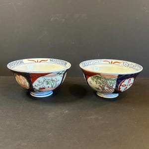May include: Two decorative ceramic bowls with intricate floral and geometric patterns. The bowls feature a white interior, a blue base, and a detailed exterior design with red, blue, and green accents. The bowls are placed side by side.