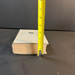 Peut inclure: Un livre bleu clair avec un embl&egrave;me vert, mesur&eacute; avec un m&egrave;tre ruban jaune. Le livre mesure environ 20 cm de haut. Les pages sont vieillies et la couverture est de couleur bleu clair.