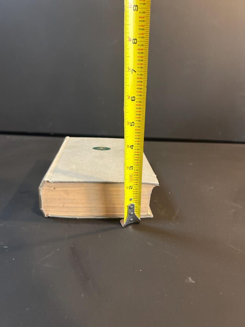 Peut inclure: Un livre bleu clair avec un embl&egrave;me vert, mesur&eacute; avec un m&egrave;tre ruban jaune. Le livre mesure environ 20 cm de haut. Les pages sont vieillies et la couverture est de couleur bleu clair.