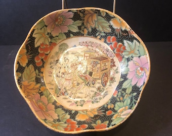 May include: A black and white porcelain bowl with a gold rim and floral design. The bowl features a scene of people riding horses and a carriage with a gold and red design.