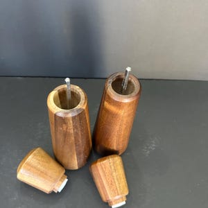 Pu&ograve; includere: Due saliere e pepiere in legno con un motivo a venature di legno marrone e marrone rossiccio. Le saliere sono aperte e i coperchi sono rimossi. I coperchi sono anche in legno e hanno un fondo in gomma bianca.