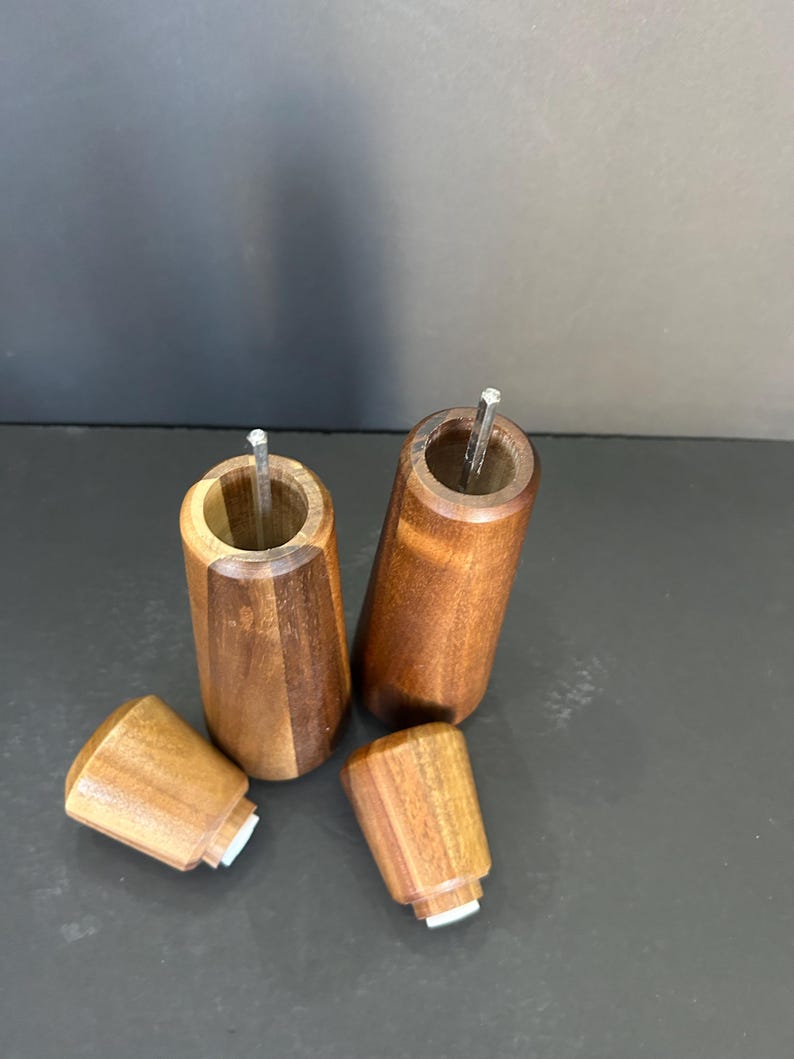 Pu&ograve; includere: Due saliere e pepiere in legno con un motivo a venature di legno marrone e marrone rossiccio. Le saliere sono aperte e i coperchi sono rimossi. I coperchi sono anche in legno e hanno un fondo in gomma bianca.