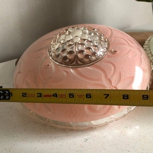 Puede incluir: Una l&aacute;mpara de techo de cristal rosa con un centro de cristal transparente y un dise&ntilde;o floral. La l&aacute;mpara tiene un di&aacute;metro de aproximadamente 23 cm.