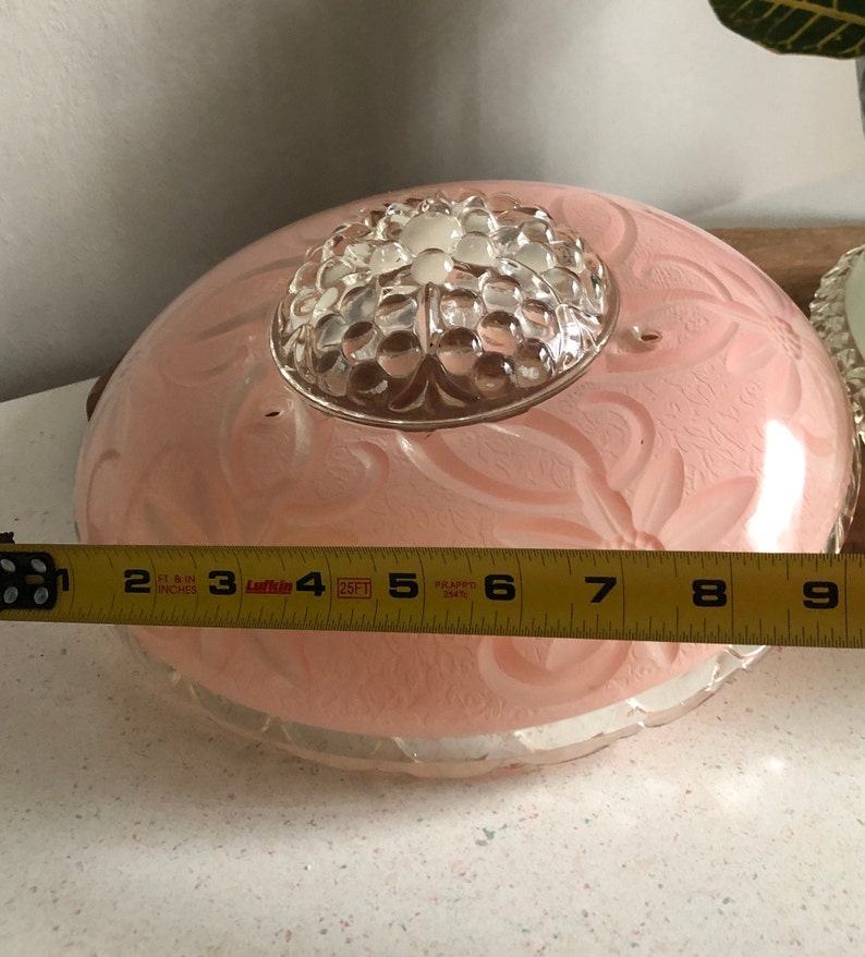 Puede incluir: Una l&aacute;mpara de techo de cristal rosa con un centro de cristal transparente y un dise&ntilde;o floral. La l&aacute;mpara tiene un di&aacute;metro de aproximadamente 23 cm.