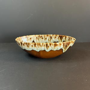 May include: A ceramic bowl with a brown exterior and a light green and brown rim. The bowl has a unique, textured design around the edge. The interior of the bowl is a solid brown color. The bowl is likely used for serving food.