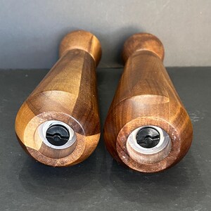 Pu&ograve; includere: Due macinini per sale e pepe in legno con finitura in legno marrone scuro. I macinini hanno una forma cilindrica con una parte superiore e inferiore leggermente rastremata. La parte inferiore di ogni macinino ha un meccanismo di macinazione in plastica nera.