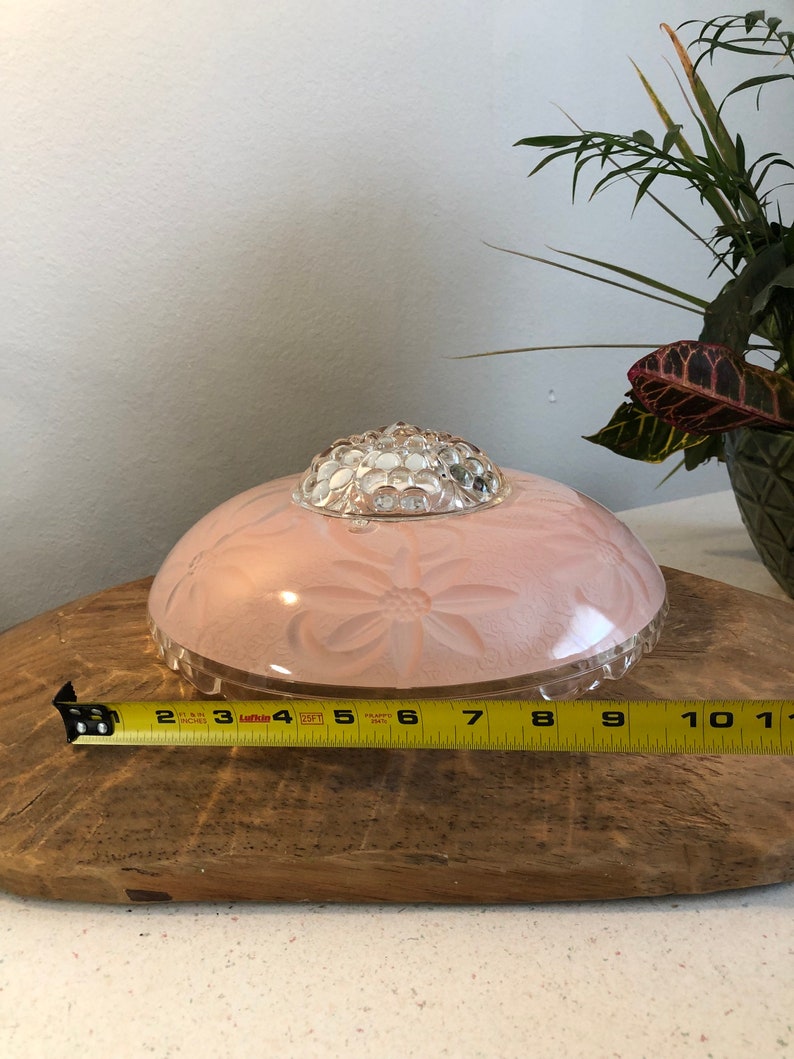 Puede incluir: Una l&aacute;mpara de techo de cristal rosa con una c&uacute;pula de cristal transparente y un dise&ntilde;o floral. La l&aacute;mpara tiene un di&aacute;metro de 15 cm.
