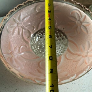 Puede incluir: Una l&aacute;mpara de techo de cristal rosa con un dise&ntilde;o floral y una pieza central de cristal transparente. La l&aacute;mpara tiene un di&aacute;metro de 25,4 cm.