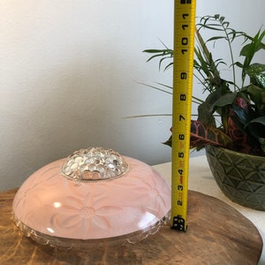 Puede incluir: Una l&aacute;mpara de techo de cristal rosa con una c&uacute;pula de cristal transparente y un dise&ntilde;o floral. La l&aacute;mpara tiene un di&aacute;metro de 18 cm.