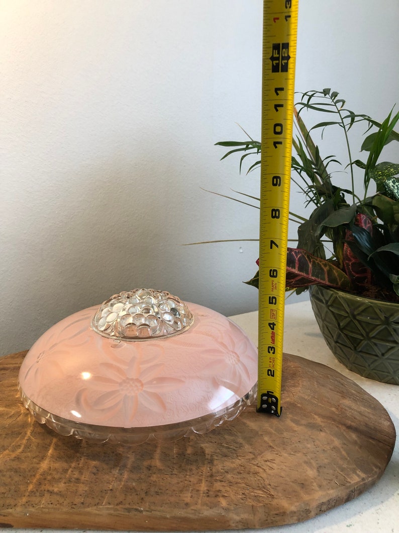 Puede incluir: Una l&aacute;mpara de techo de cristal rosa con una c&uacute;pula de cristal transparente y un dise&ntilde;o floral. La l&aacute;mpara tiene un di&aacute;metro de 18 cm.