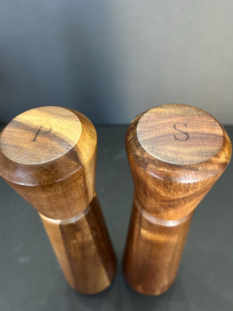 Pu&ograve; includere: Un set di due macinini per sale e pepe in legno con finitura marrone scuro. I macinini sono incisi con le lettere "P" e "S" sulla parte superiore.