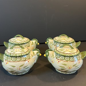 May include: Set of four ceramic chicken-shaped casserole dishes with lids. The dishes are decorated with green and white floral patterns and have a rustic, farmhouse style.