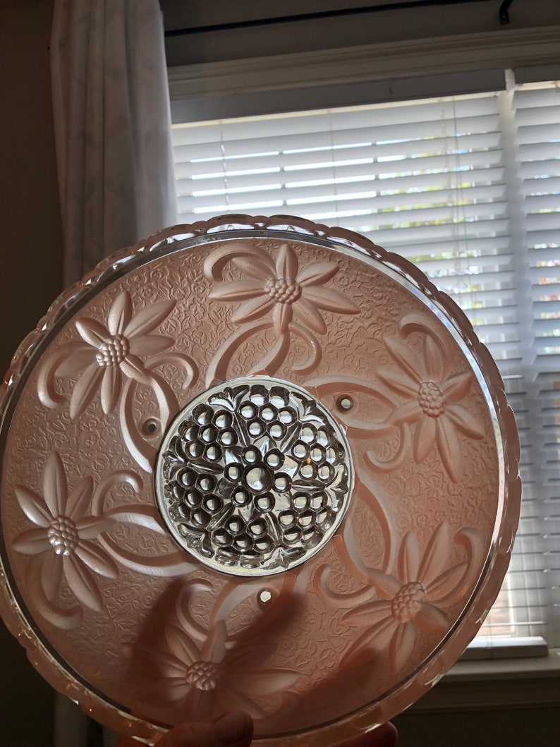 Puede incluir: Una l&aacute;mpara de techo de cristal rosa con un dise&ntilde;o floral y un centro de cristal transparente.