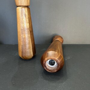 Pu&ograve; includere: Due macinini per sale e pepe in legno con finitura marrone scuro. I macinini sono in legno e hanno un design semplice. Il fondo di un macinino &egrave; visibile, mostrando una vite.