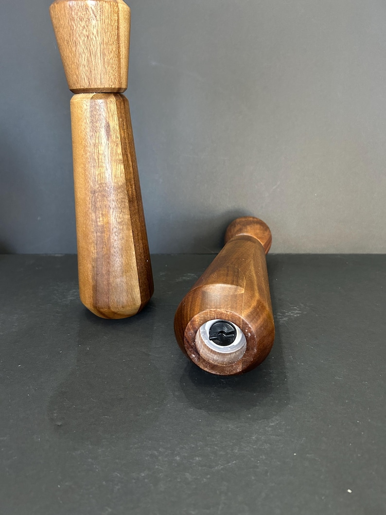 Pu&ograve; includere: Due macinini per sale e pepe in legno con finitura marrone scuro. I macinini sono in legno e hanno un design semplice. Il fondo di un macinino &egrave; visibile, mostrando una vite.