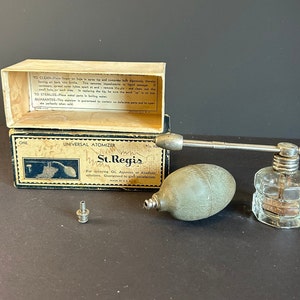 Pode incluir: Um atomizador universal vintage St. Regis na sua caixa original. O atomizador é feito de vidro e metal e tem um bulbo para dispensar líquido. A caixa é feita de cartão e tem um rótulo com instruções de uso. O atomizador é um ótimo exemplo de equipamento médico vintage.