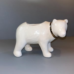 May include: White ceramic polar bear planter with a gold trim around the neck. The planter has a hollowed-out top for planting.