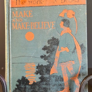 Pode incluir: Uma capa de livro vintage com fundo azul e texto laranja. O título é "The Work-Play Books" e "MAKE AND MAKE-BELIEVE". A capa apresenta uma ilustração de uma pessoa em uma paisagem com um pôr do sol.
