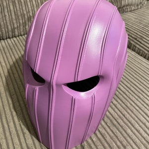 May include: A purple helmet with vertical ridges and eye holes. The helmet is made of a smooth, hard material.