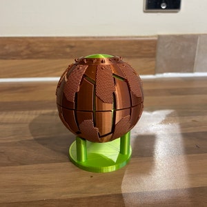 May include: A 3D printed sphere with a textured surface, in a copper colour, on a green stand.