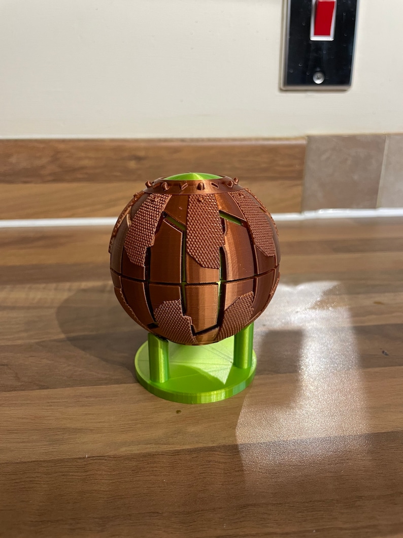 May include: A 3D printed sphere with a textured surface, in a copper colour, on a green stand.