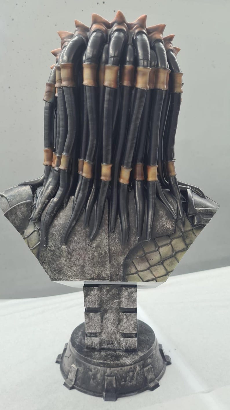 Puede incluir: Busto detallado de un alien&iacute;gena Predator, con rastas negras y detalles en marr&oacute;n. La escultura tiene un aspecto met&aacute;lico envejecido con intrincados detalles de armadura. Montado sobre una base geom&eacute;trica texturizada.