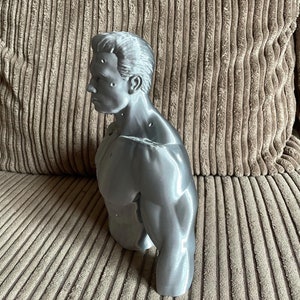 May include: A silver-colored 3D printed bust of a man with a muscular physique. The bust is detailed with defined muscles and a realistic facial expression.