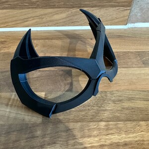 Puede incluir: Una m&aacute;scara de pl&aacute;stico negro con un dise&ntilde;o geom&eacute;trico, que se asemeja a una m&aacute;scara de superh&eacute;roe.