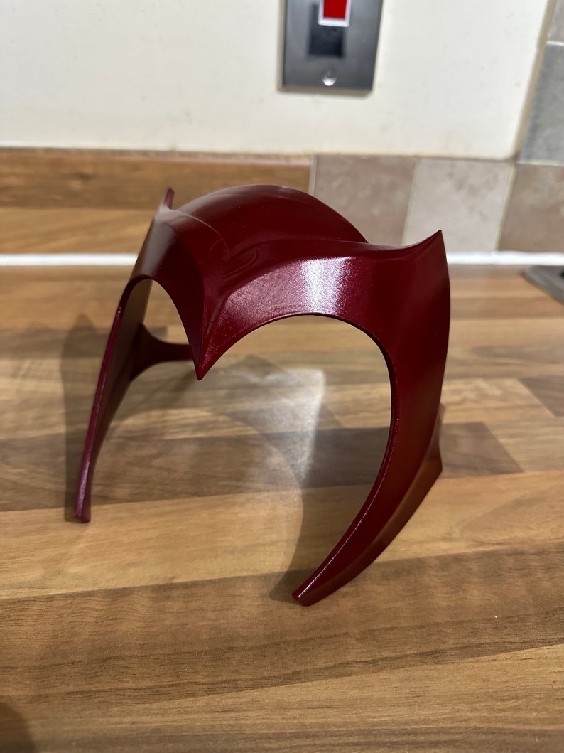 May include: A burgundy red plastic headband with a curved design. The headband is made of a smooth, glossy material.