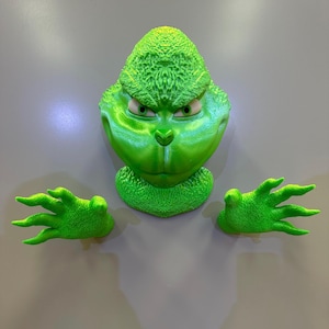 May include: A green Grinch head and two green Grinch hands. The Grinch is a fictional character from the Dr. Seuss book How the Grinch Stole Christmas.