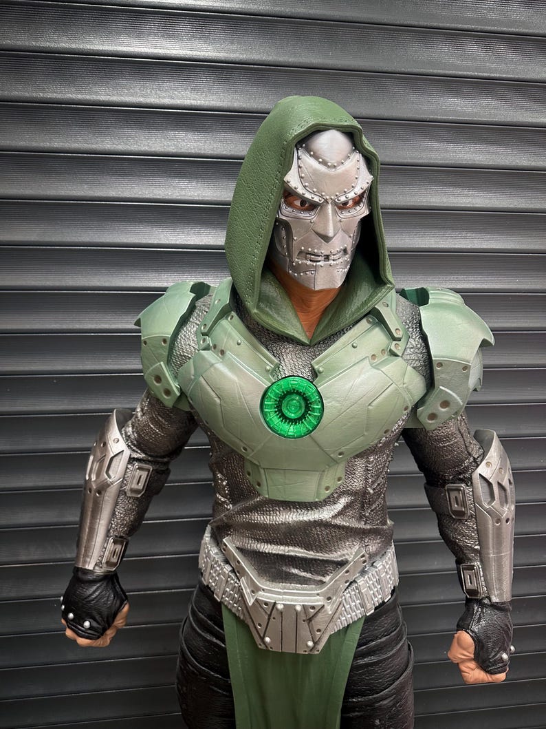 May include: A detailed action figure of a character in a green and silver armored suit with a silver mask and green hood. The figure has a glowing green chest emblem and black gloves. The background is a gray, slatted surface.
