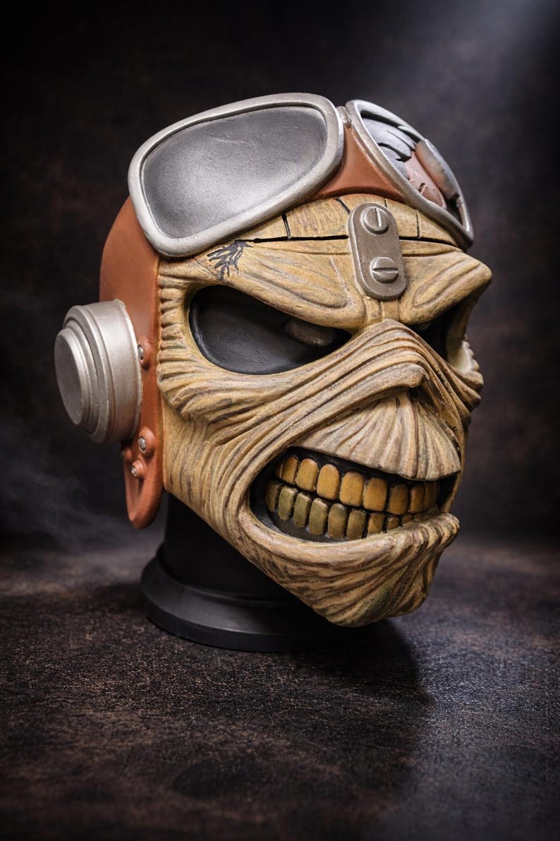 May include: A detailed sculpture of a skull with a menacing expression, featuring a weathered, textured appearance. The skull wears aviator goggles and a brown leather helmet. The teeth are a golden color, and the overall design is reminiscent of a rock and roll theme.
