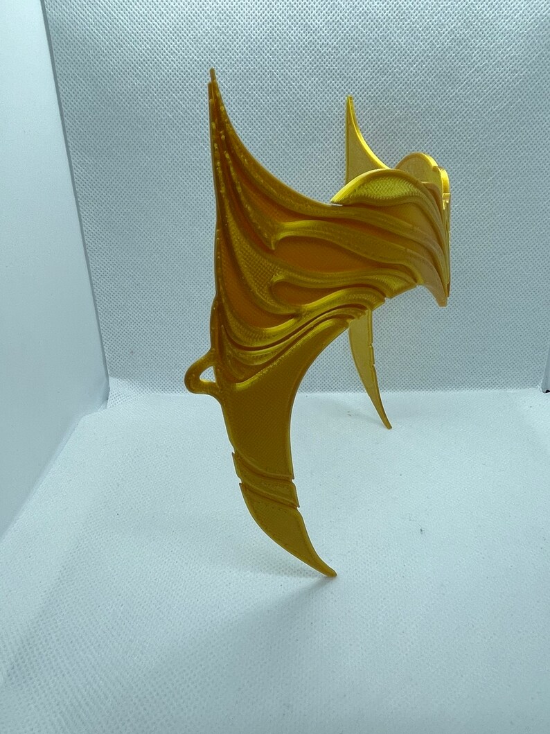 May include: A gold-coloured, 3D printed crown with a decorative, intricate design. The crown is made of plastic and has a smooth, shiny finish.