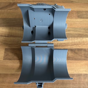 May include: A grey 3D printed object with a hinged lid and a small lever. The object is open and the inside is visible.