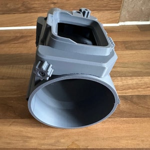 May include: A grey 3D printed camera cage with a round opening at the bottom and a rectangular opening at the top. The cage has two adjustable knobs on the side.