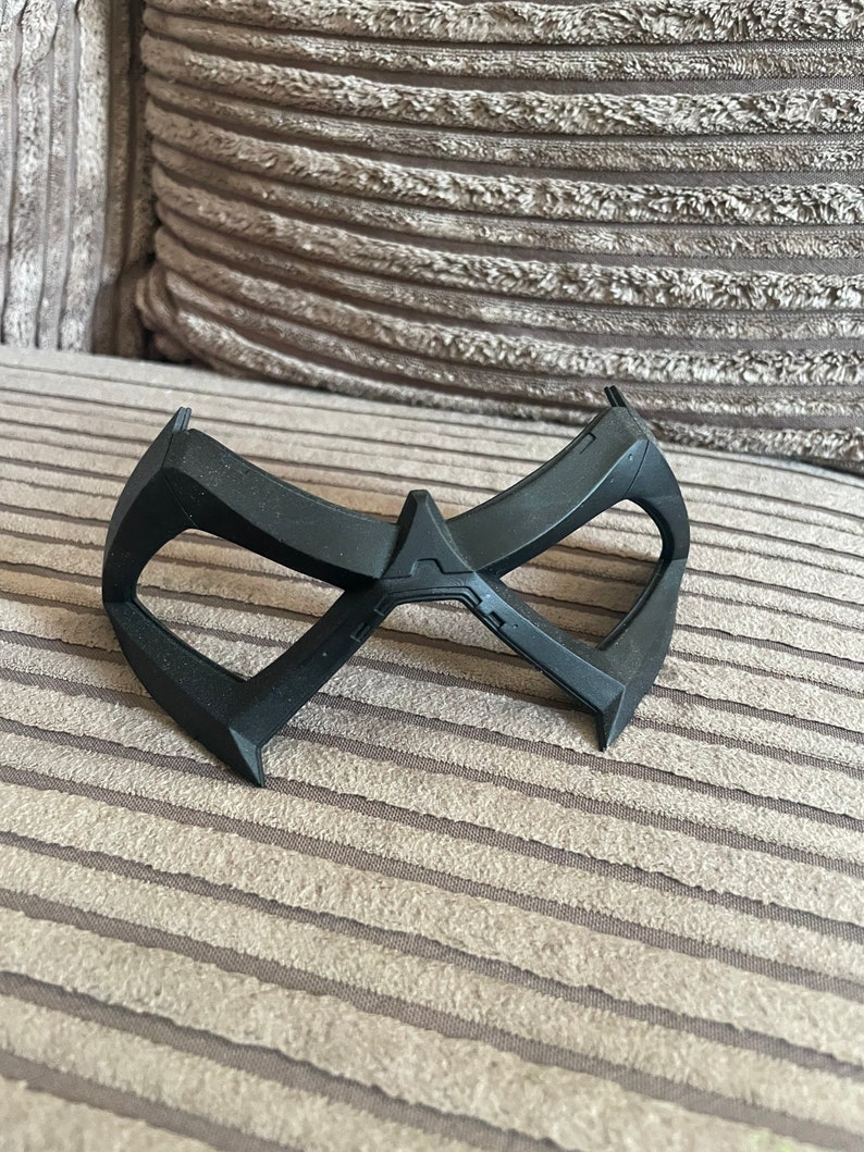 May include: A black plastic mask with a distinctive design, resembling a superhero's mask.