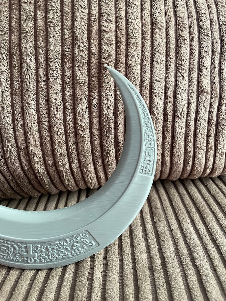 May include: A white crescent moon-shaped object with intricate designs on the surface. The object is made of a smooth, plastic-like material.