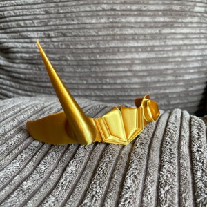 May include: A gold-colored crown with a pointed tip, resting on a gray textured surface.